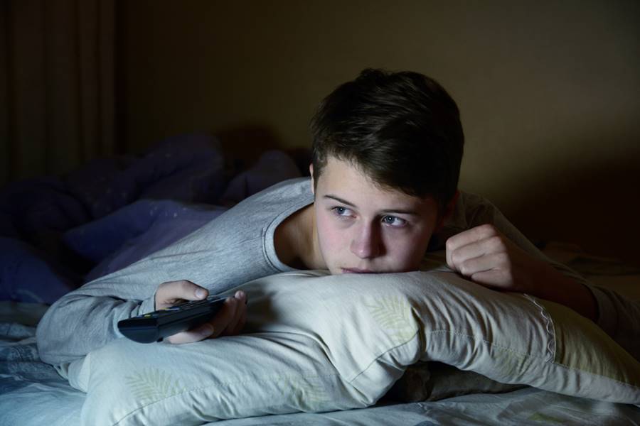 Menino deitado na cama assistindo à séries